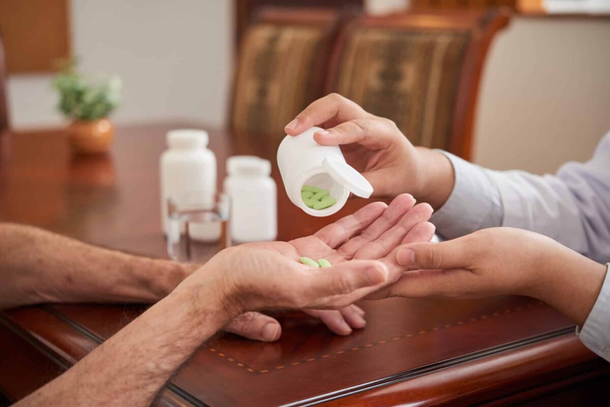 Crop shot of doctor putting pills in hand of senior man sitting at table, therapy and medication massachusetts