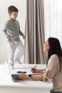 woman working while son is playing on her desk, parenting in massachusetts
