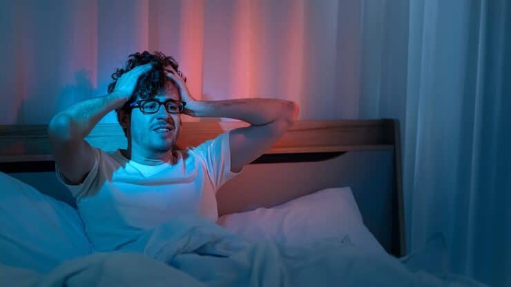 Young man lying awake in bed, looking restless and unable to fall asleep due to stress and anxiety