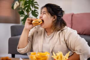Happy Asian fat woman enjoy eating delicious hamburger on living room. eating disorder behaviors massachusetts