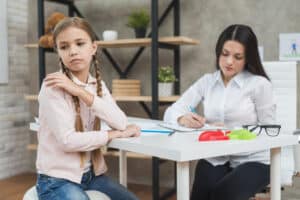 Psychologist writing notes on clipboard during meeting with her depressed girl, psychiatrist for teens in massachusetts