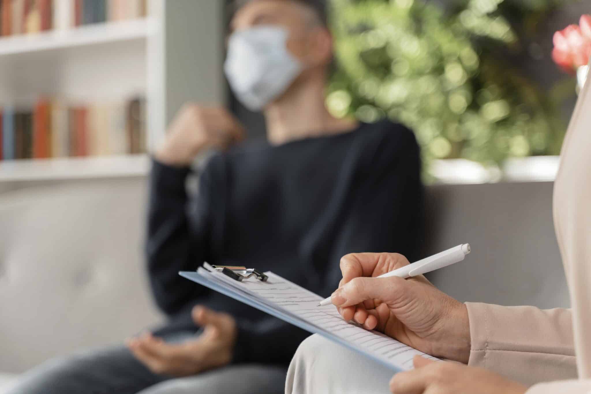 Woman therapist taking notes of man in therapy office with mask, psychiatrist appointment massachusetts