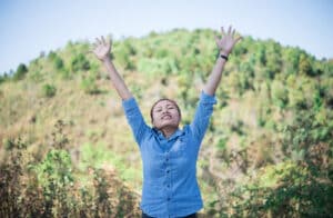 Young woman standing looking to a sky with raised hands while during hike in the mountain, psychopharmacology massachusetts