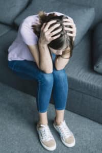 Young woman suffering from headache sitting on sofa, anxiety and trauma massachusetts