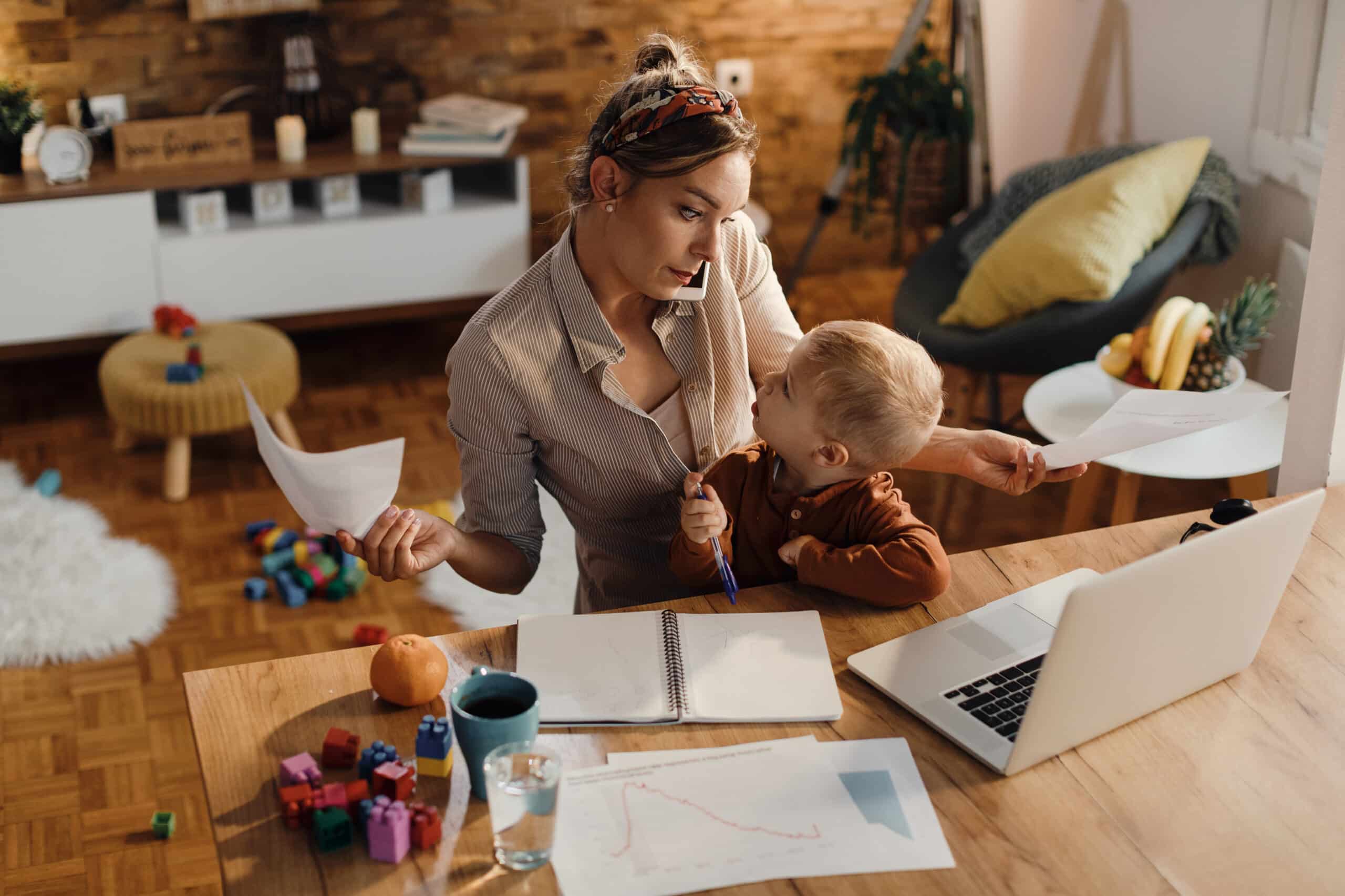 Working parent burnout and anxiety after parental leave Massachusetts, multitasking at home while holding a child and checking emails, showing stress